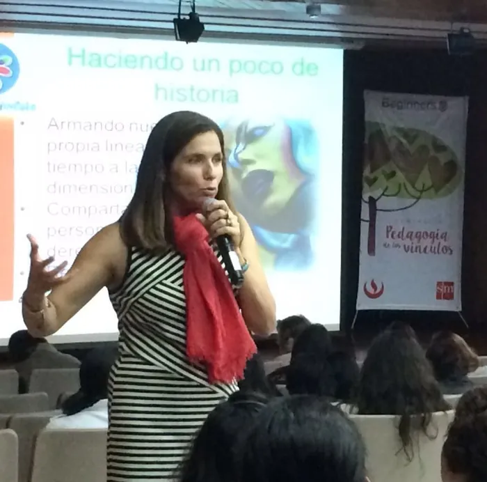 Trini Ried con un micrófono, dando una charla frente a un auditorio; detrás, un pendón que dice «Pedagogía de los vínculos»